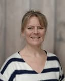 Mirjam Schmidt-Erftemeijer, StudieKeuzeCoach in 't Gooi, lachend in een gestreepte trui voor een lichte houten wand
