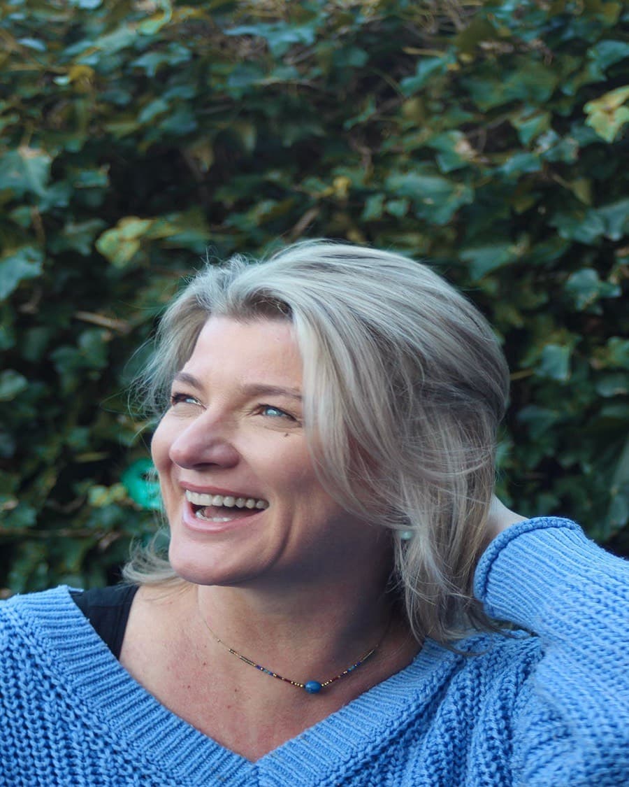 Silvia Dragt, StudieKeuzeCoach in Leiden, lachend in een blauwe gebreide trui voor een haag van klimop