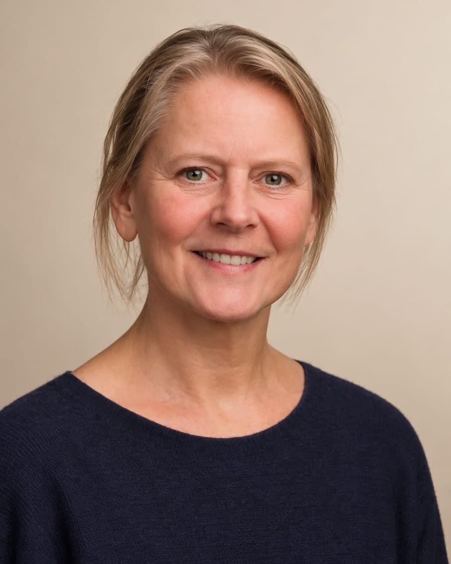 Mirjam Schmidt-Erftemeijer, StudieKeuzeCoach in 't Gooi, lachend in een gestreepte trui voor een lichte houten wand