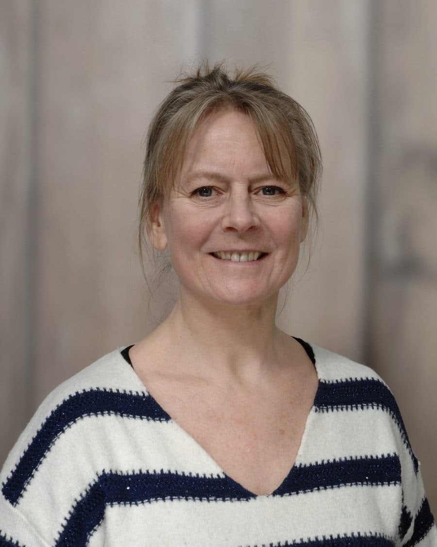 Mirjam Schmidt-Erftemeijer, StudieKeuzeCoach in 't Gooi, lachend in een gestreepte trui voor een lichte houten wand